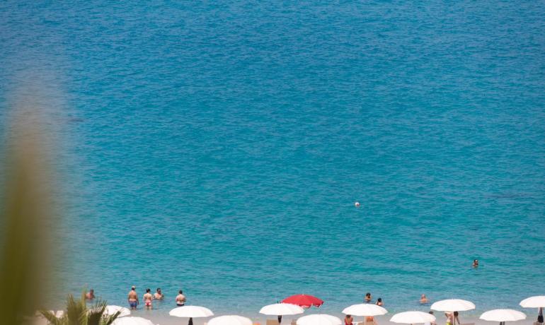 Beach with white umbrellas and people swimming in clear blue sea.