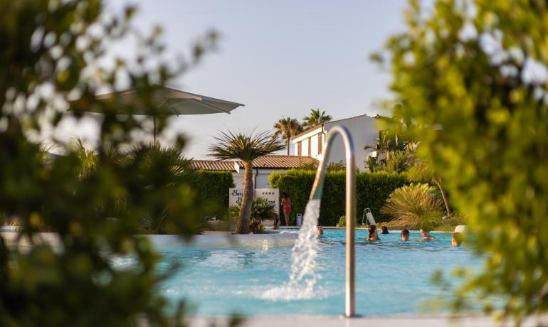 Outdoor pool with people swimming, surrounded by plants and umbrellas.