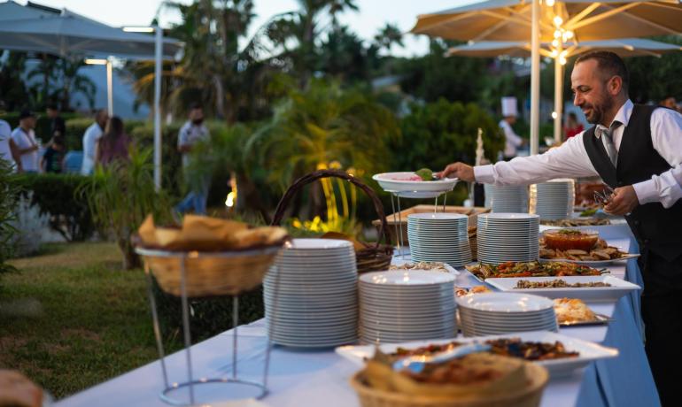 Outdoor buffet with various dishes and a waiter serving.