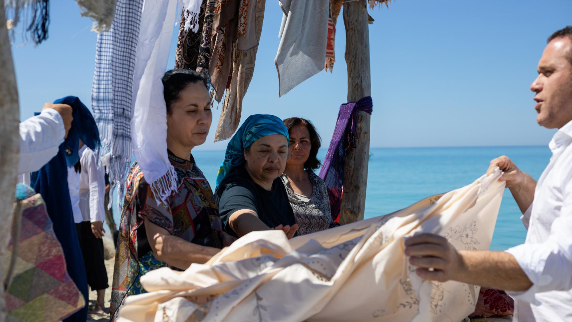 People looking at fabrics hanging near the sea.