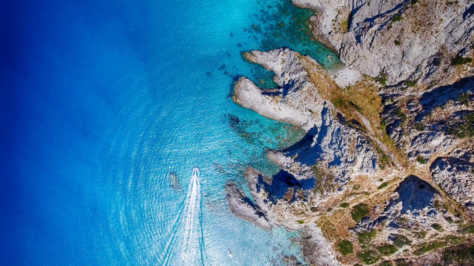 Vista aerea di una barca che naviga in acque cristalline vicino a scogliere rocciose.