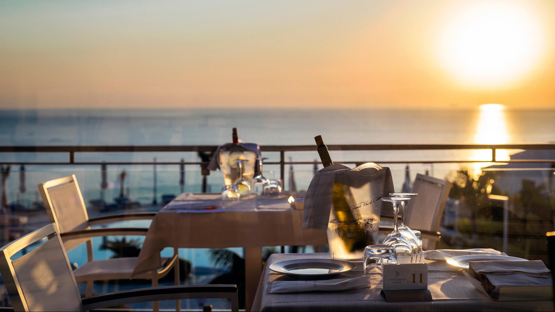 Romantic sunset dinner with sea view, wine, and glasses.