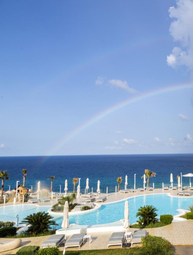 Pool with sea view and rainbow at a tropical resort.