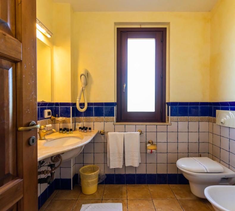 Bagno con piastrelle blu, finestra, lavandino, WC e bidet.