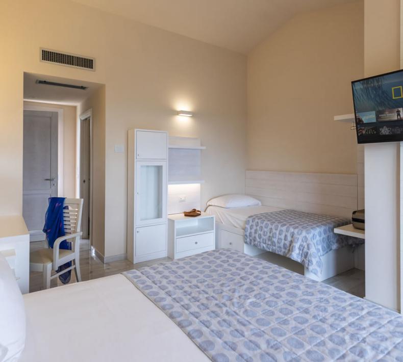 Camera d'albergo con letto matrimoniale e singolo, TV e arredamento moderno.