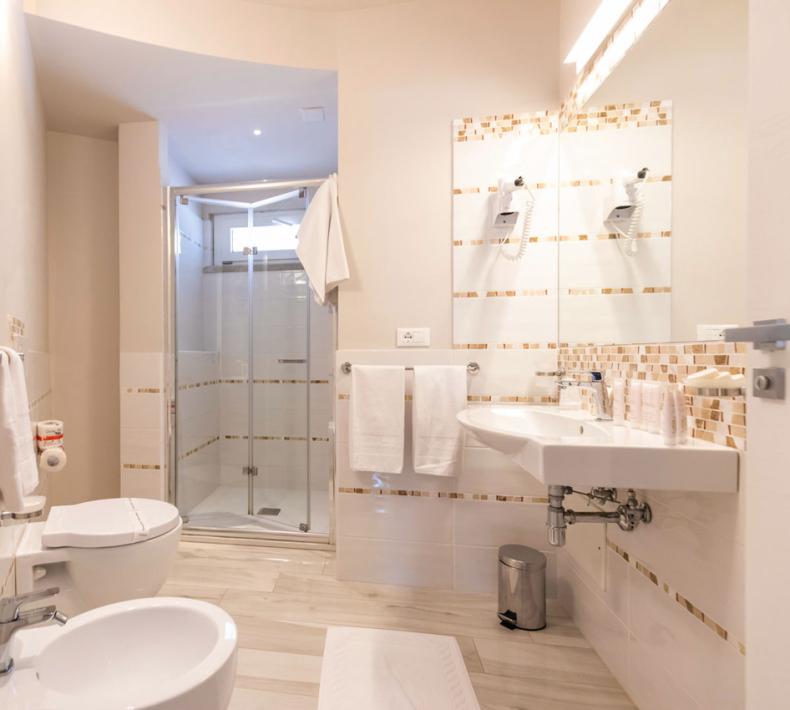 Modern bathroom with shower, bidet, and sink, decorated with tiles and white towels.