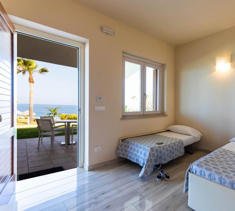 Chambre lumineuse avec deux lits simples, vue sur la mer et terrasse.