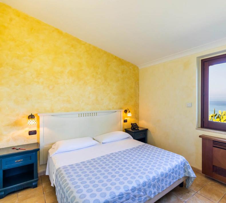 Gemütliches Zimmer mit Meerblick, gelben Wänden und Doppelbett.