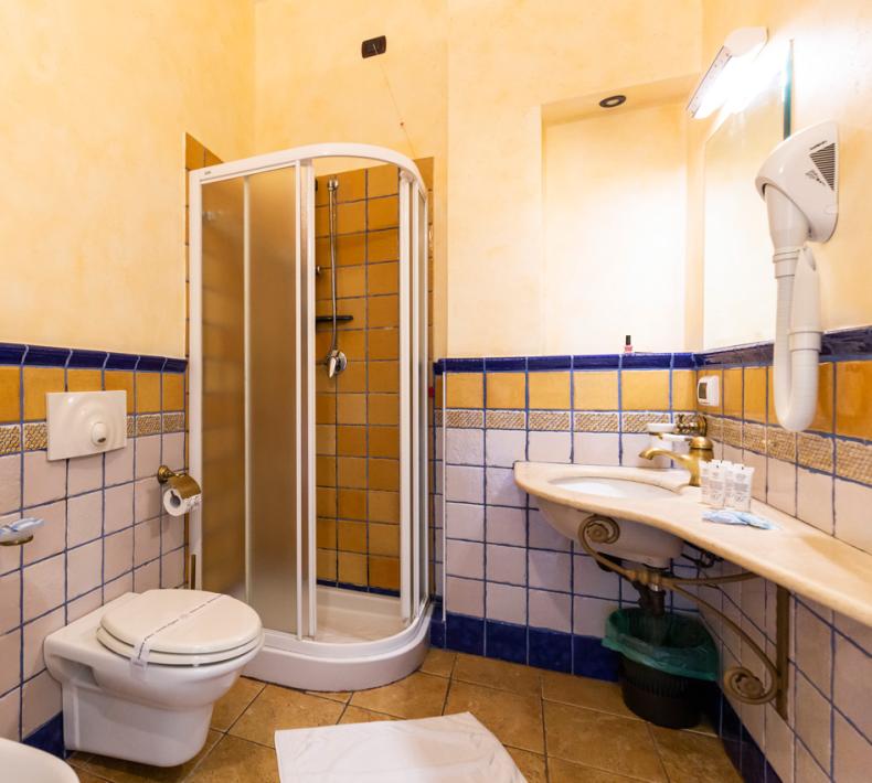 Bathroom with shower, sink, bidet, toilet, and hairdryer, tiled in yellow and blue.