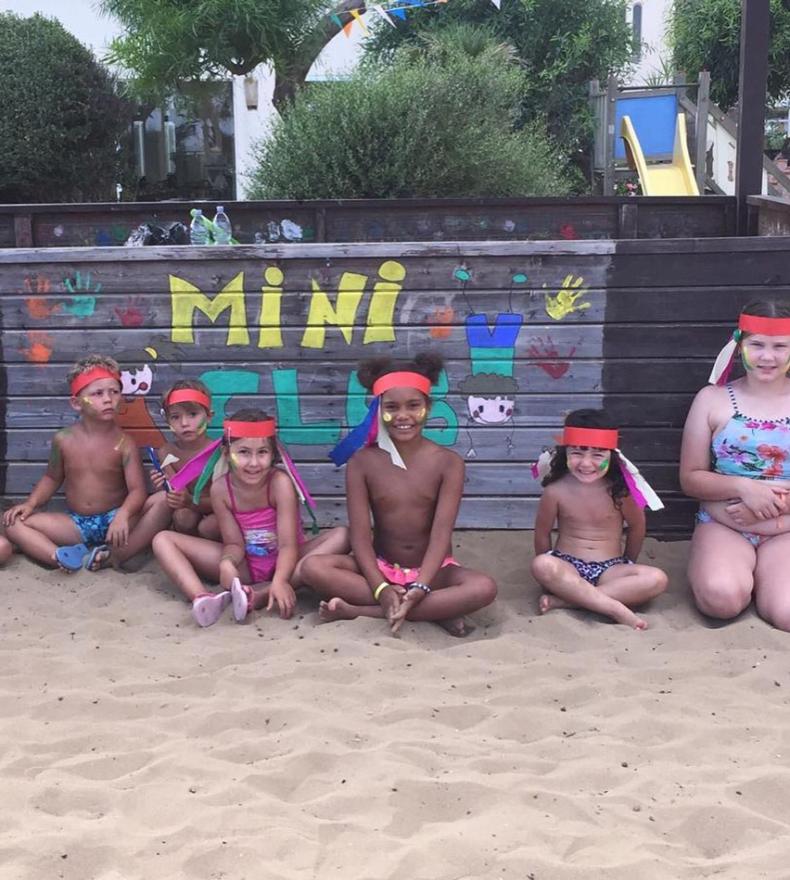 Enfants souriants sur la plage avec des bandeaux colorés au Mini Club.