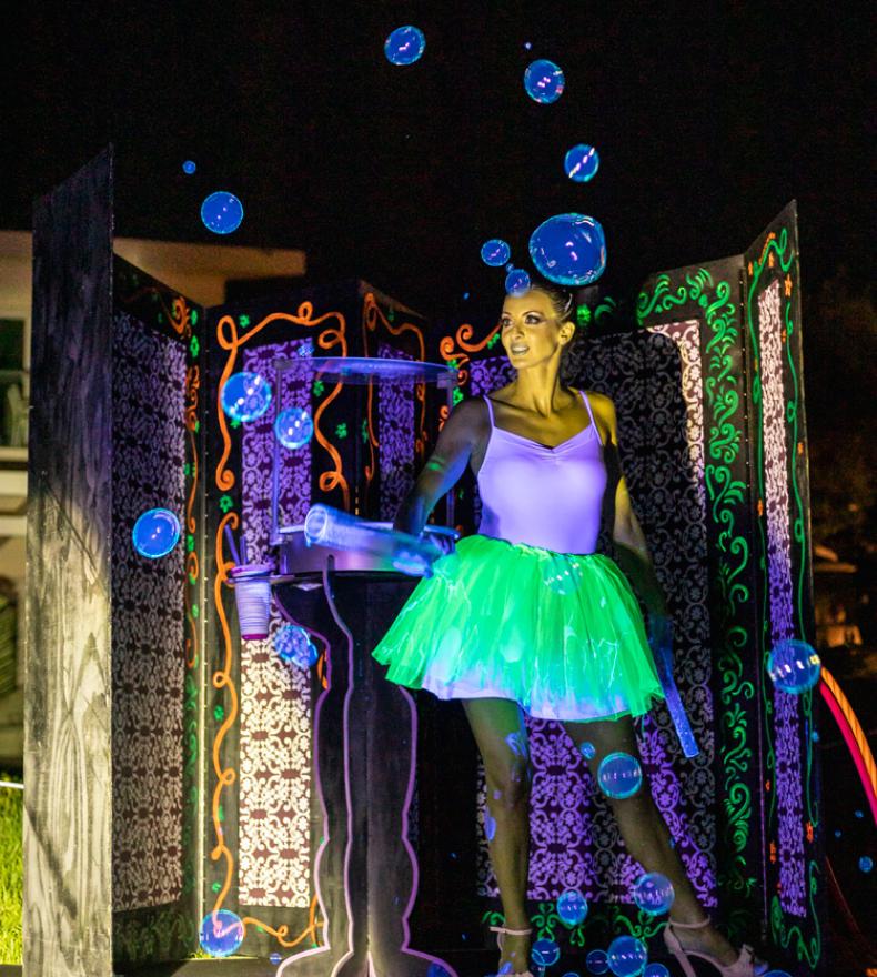 Woman with fluorescent tutu makes soap bubbles in a nighttime show.