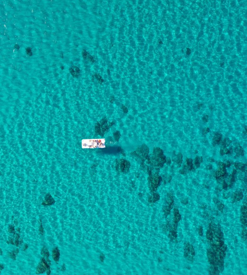 Aerial view of a boat and a swimmer in crystal-clear sea.