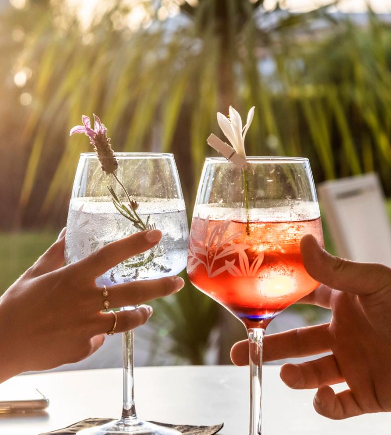 Two people toasting with colorful cocktails at sunset.