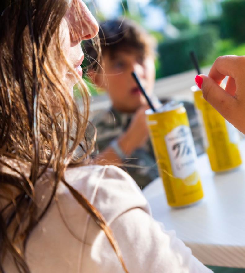 Two people drinking yellow beverages with black straws outdoors.