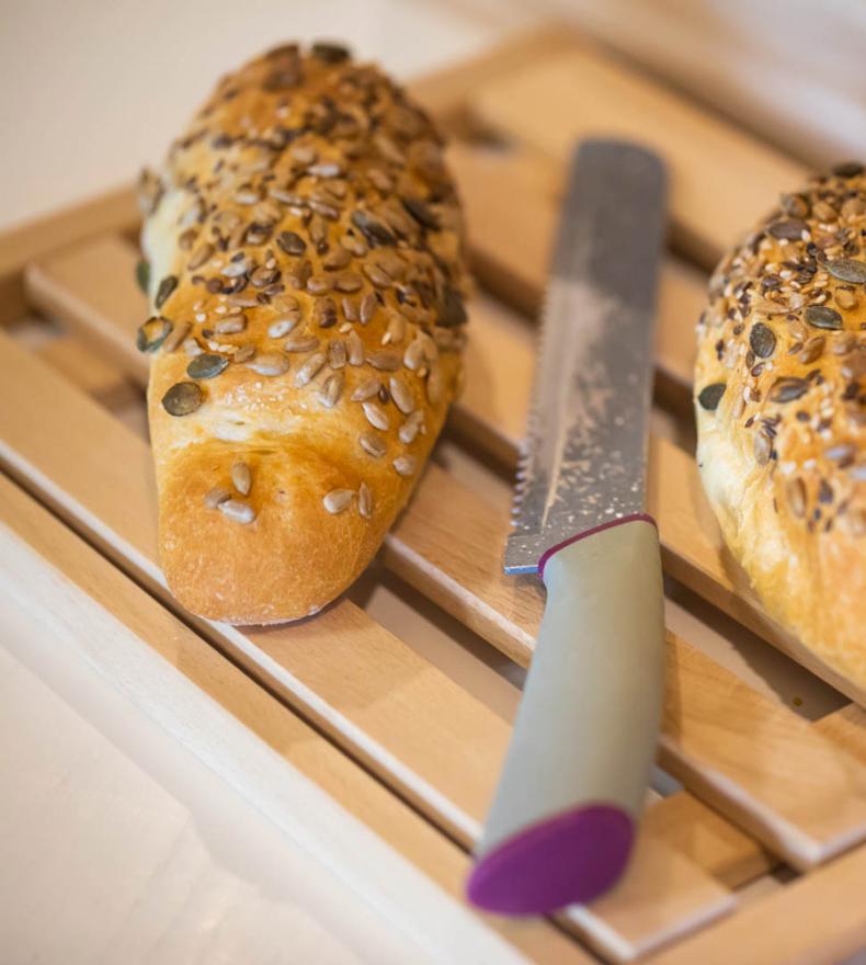 Two seeded rolls and a knife on a wooden cutting board.