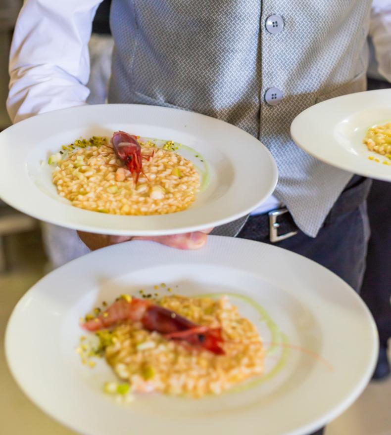 Waiter serves risotto with red shrimp on white plates.