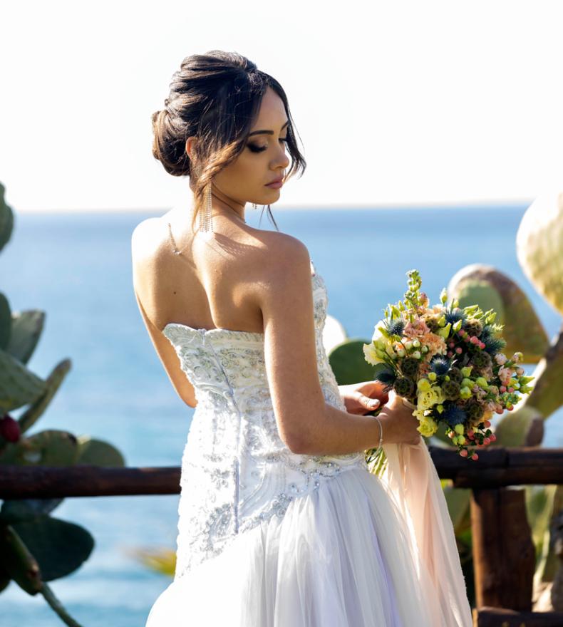 Sposa in abito bianco con bouquet, sfondo marino.