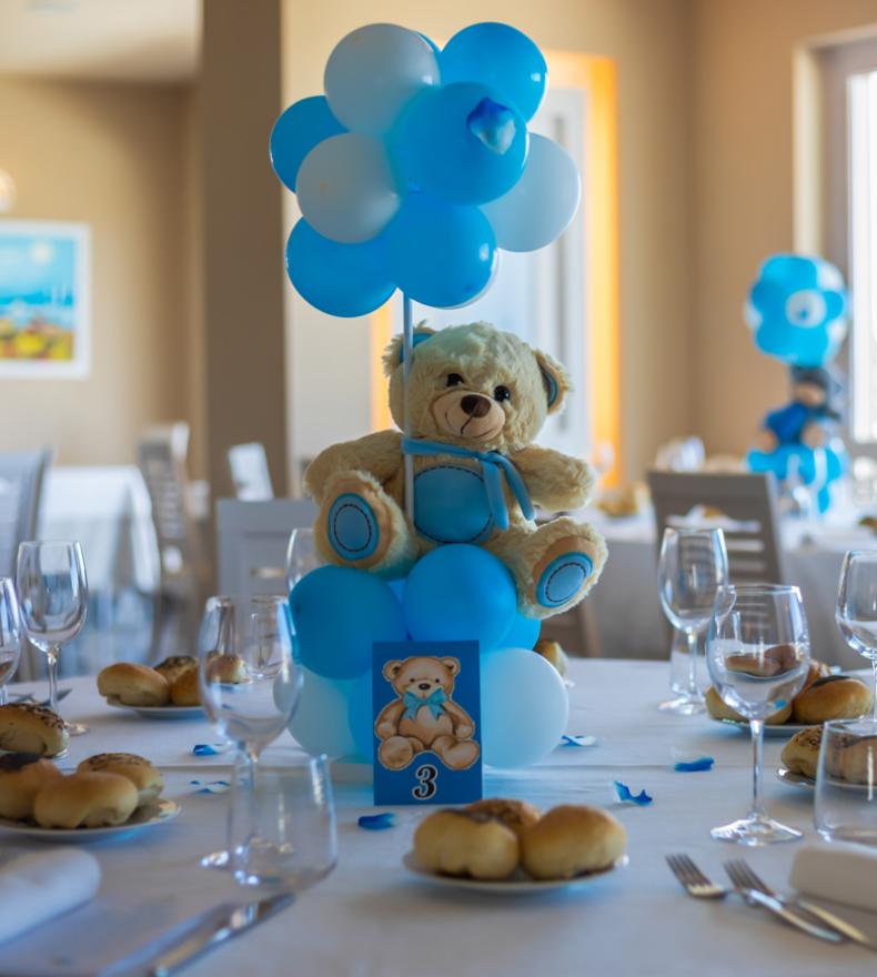 Tavolo decorato con orsetto e palloncini blu per una festa.