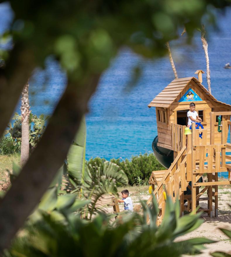 Children playing in a wooden playhouse by the sea.
