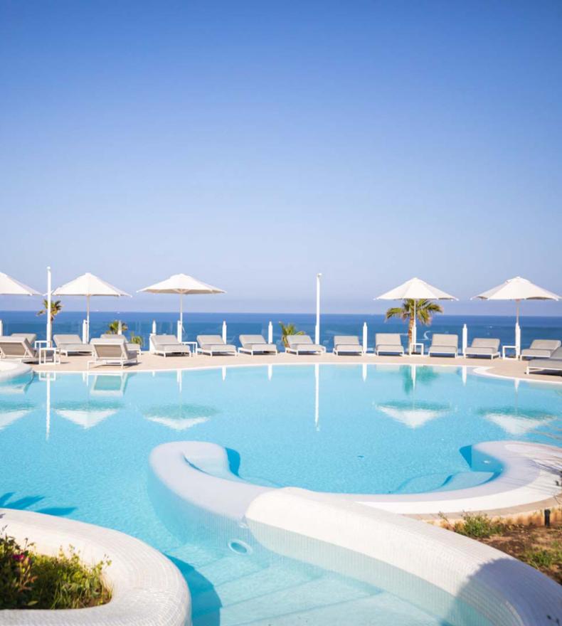 Panoramic pool with sea view and sunbeds under white umbrellas.