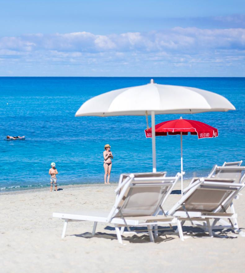 Spiaggia sabbiosa con ombrelloni, sedie a sdraio e bagnanti in mare.