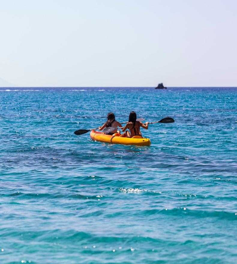 Two people in a yellow kayak on blue sea with an island in the distance.