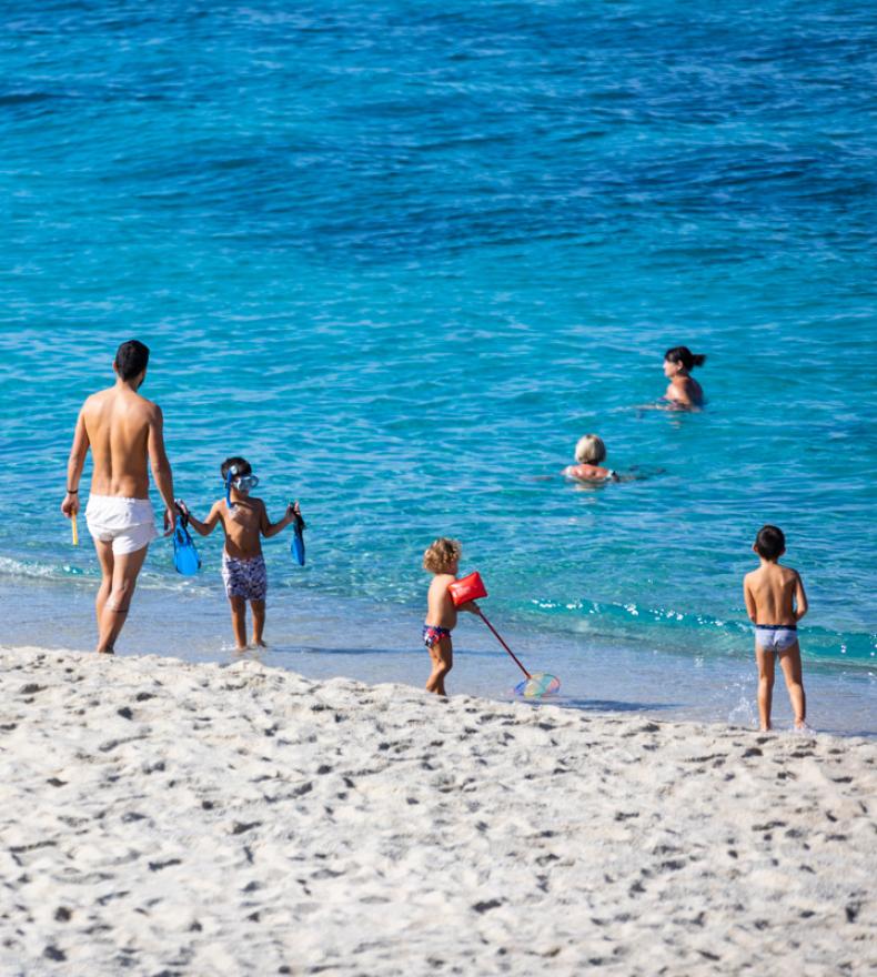 Families play on the beach and swim in the blue sea.